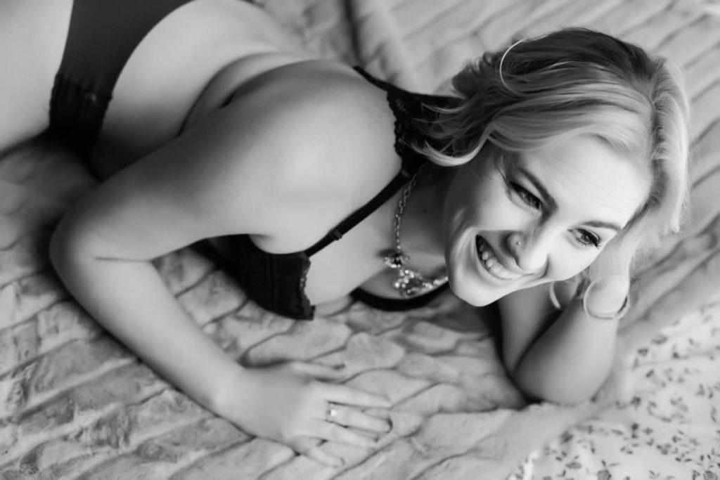 Boudoir photo of a woman smiling and lying on a bed
